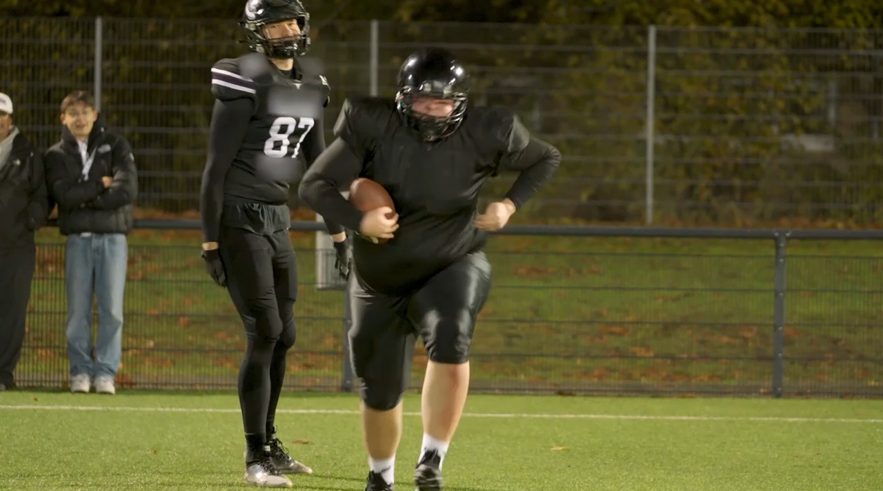 Reeze läuft in Football-Schutzkleidung über ein Spielfeld mit einem Football in der Hand. (Quelle: BSI) Reeze läuft in Football-Schutzkleidung über ein Spielfeld mit einem Football in der Hand.