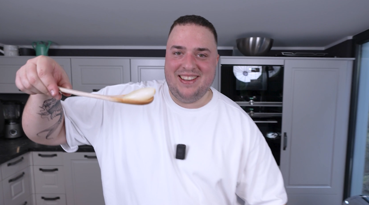 Youtuber Reeze steht in einer Küche und hält lächelnd einen Kochlöffel mit einem Zwiebelstück darauf in die Kamera. (Quelle: BSI) Youtuber Reeze steht in einer Küche und hält lächelnd einen Kochlöffel mit einem Zwiebelstück darauf in die Kamera.