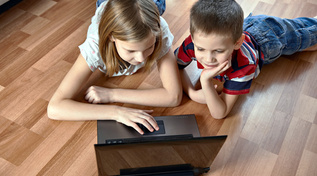 Zwei Kinder liegend auf dem Boden vor einem Laptop. (Quelle: © Sergey Ryzhov / Fotolia.com) Zwei Kinder liegend auf dem Boden vor einem Laptop.