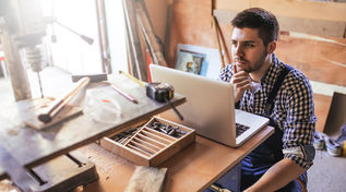 Handwerker in seiner Werkstatt mit Blick auf den Laptop (Quelle: © bernardbodo / Fotolia.com) Handwerker in seiner Werkstatt mit Blick auf den Laptop