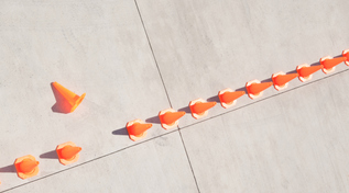 Reihe von Leitkegeln. Einer ist umgefallen und liegt ausserhalb der Reihe (Quelle: © Martin Barraud_OJO Images / iStock / GettyImages) Reihe von Leitkegeln. Einer ist umgefallen und liegt ausserhalb der Reihe