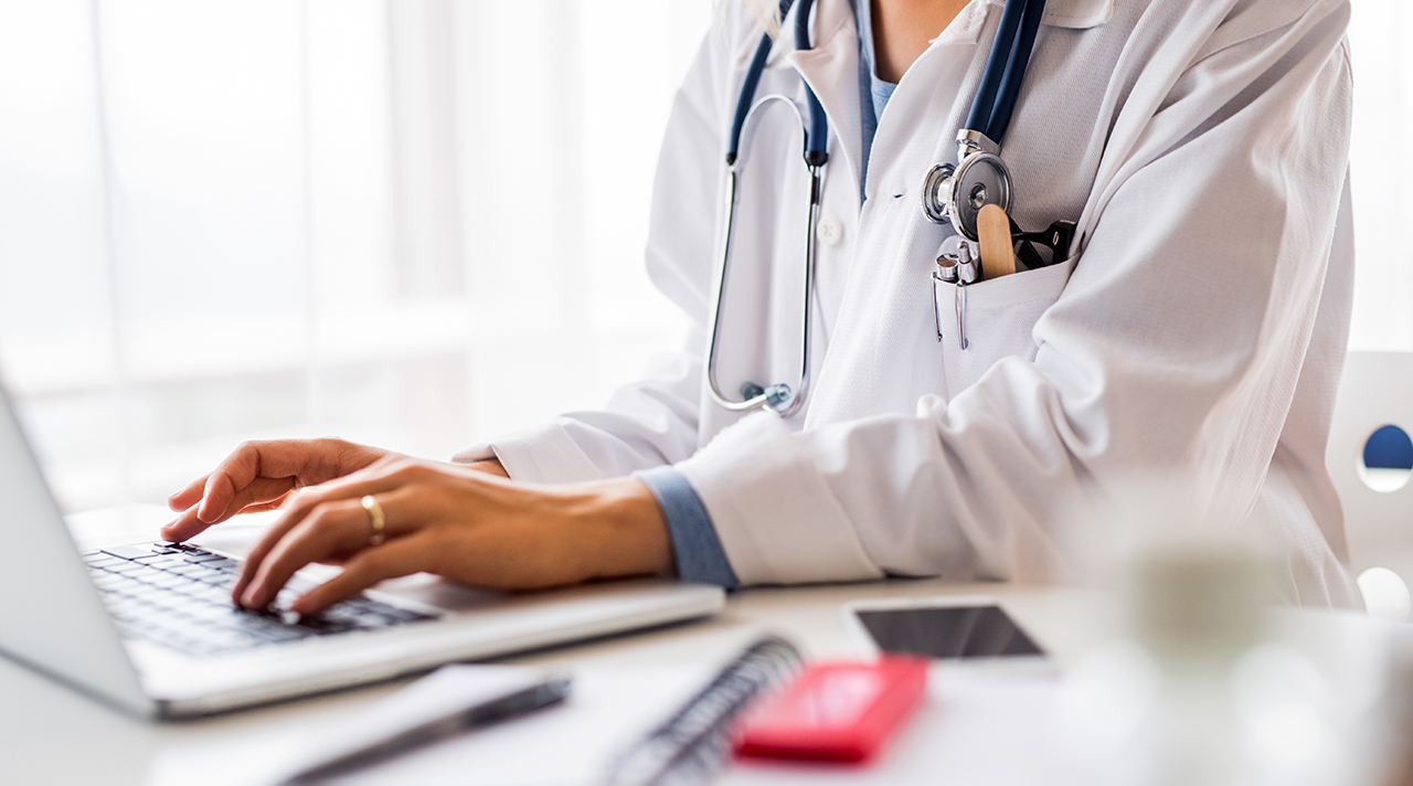 Eine Ärztin im weißen Kittel mit Stethoskop tippt auf der Tastatur eines Laptops. (Quelle: © Halfpoint / Adobe Stock) Eine Ärztin im weißen Kittel mit Stethoskop tippt auf der Tastatur eines Laptops.
